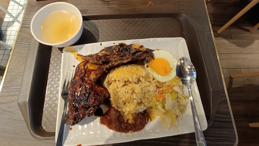 A delicious plate of Indonesian BBQ chicken with rice, fried egg, vegetables, and a side of soup.