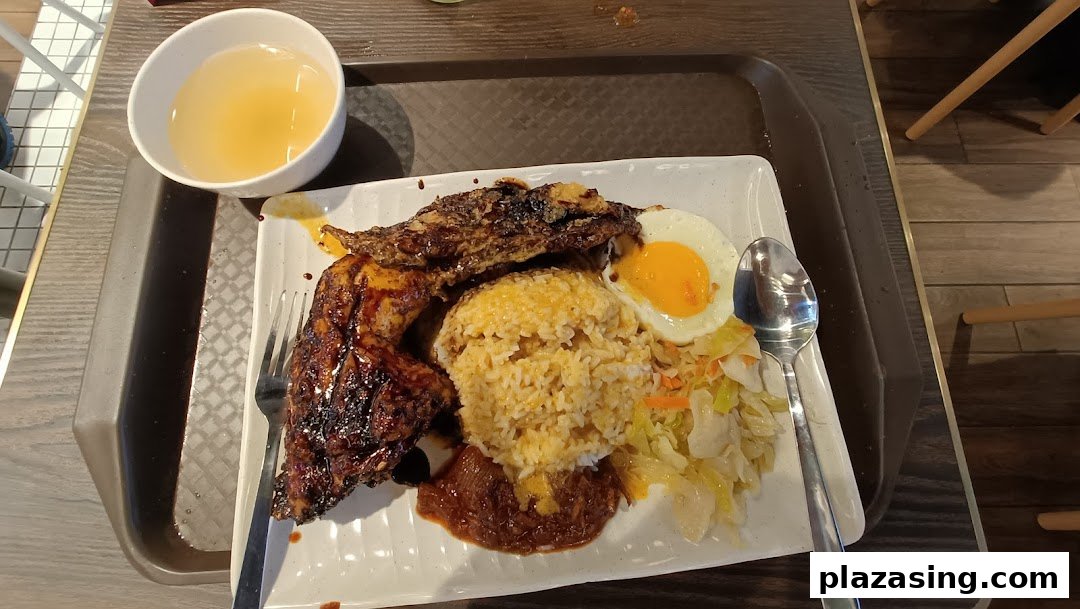 A delicious plate of Indonesian BBQ chicken with rice, fried egg, vegetables, and a side of soup.