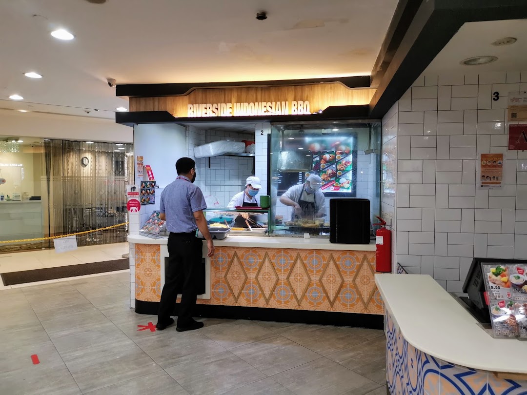 A chef prepares food at Riverside Indonesian BBQ, with a customer waiting at the counter.