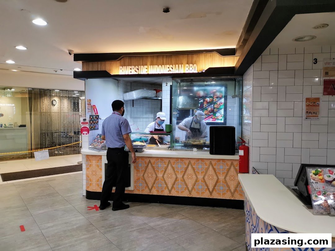 A chef prepares food at Riverside Indonesian BBQ, with a customer waiting at the counter.