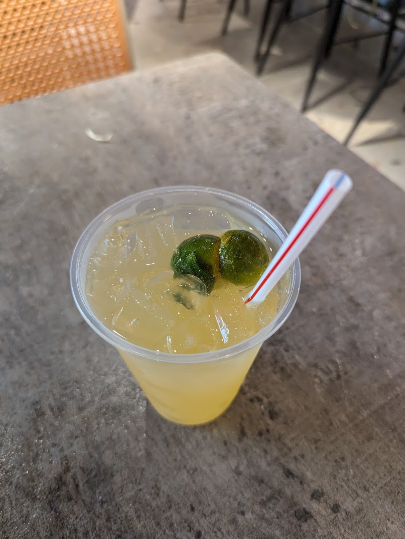 A refreshing drink with ice and lime slices in a plastic cup on a textured table.