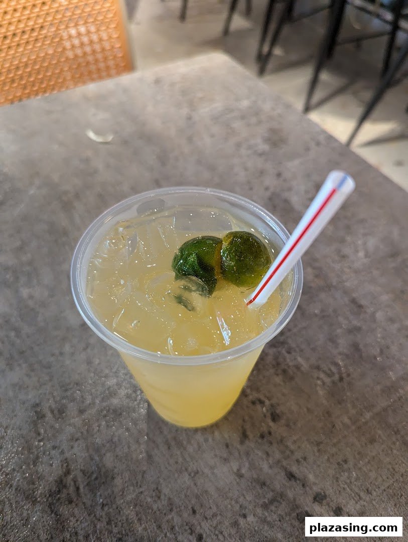 A refreshing drink with ice and lime slices in a plastic cup on a textured table.