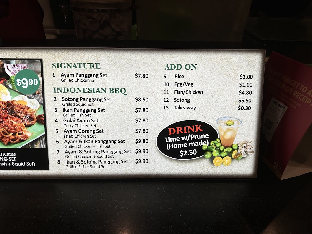 A brightly lit menu board displaying Indonesian BBQ sets, add-ons, and a homemade drink.