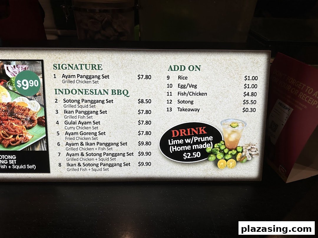 A brightly lit menu board displaying Indonesian BBQ sets, add-ons, and a homemade drink.