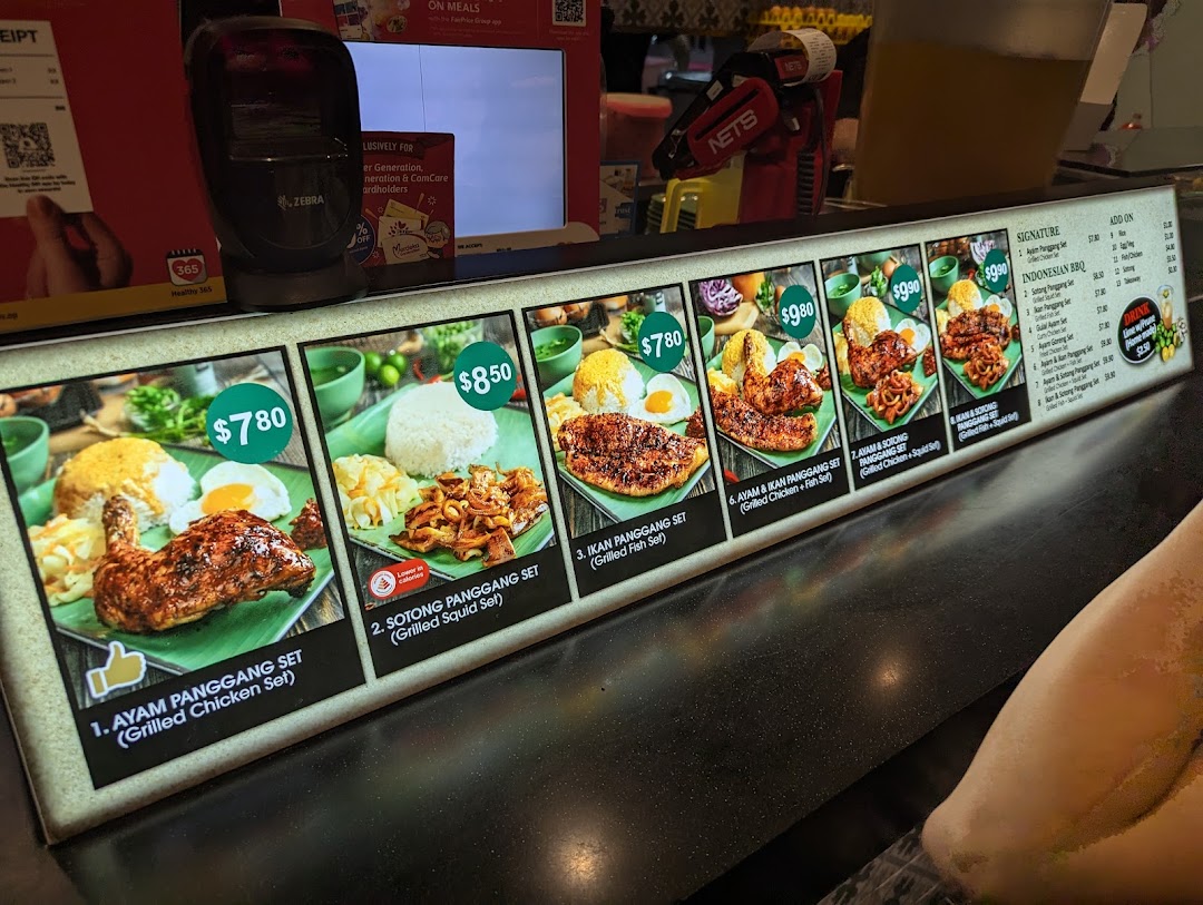 A brightly lit menu board displaying various Indonesian BBQ sets with prices and images.