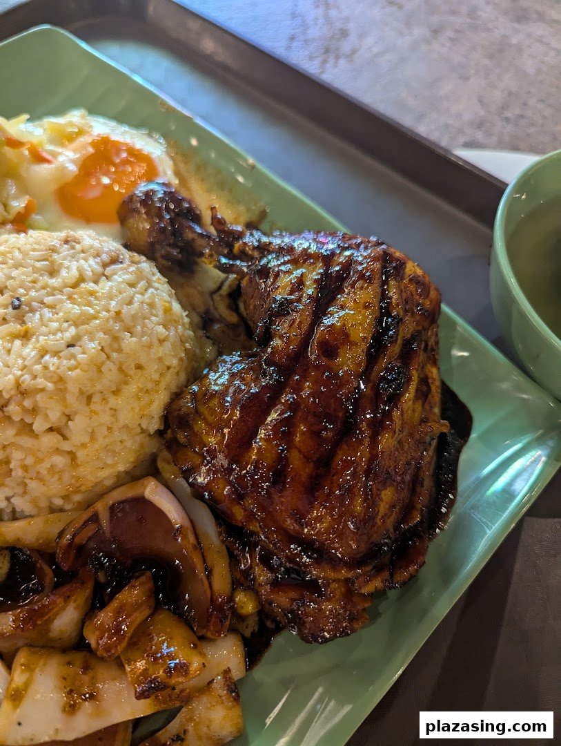 A delicious plate featuring grilled chicken, rice, squid, and a fried egg from Riverside Indonesian BBQ.