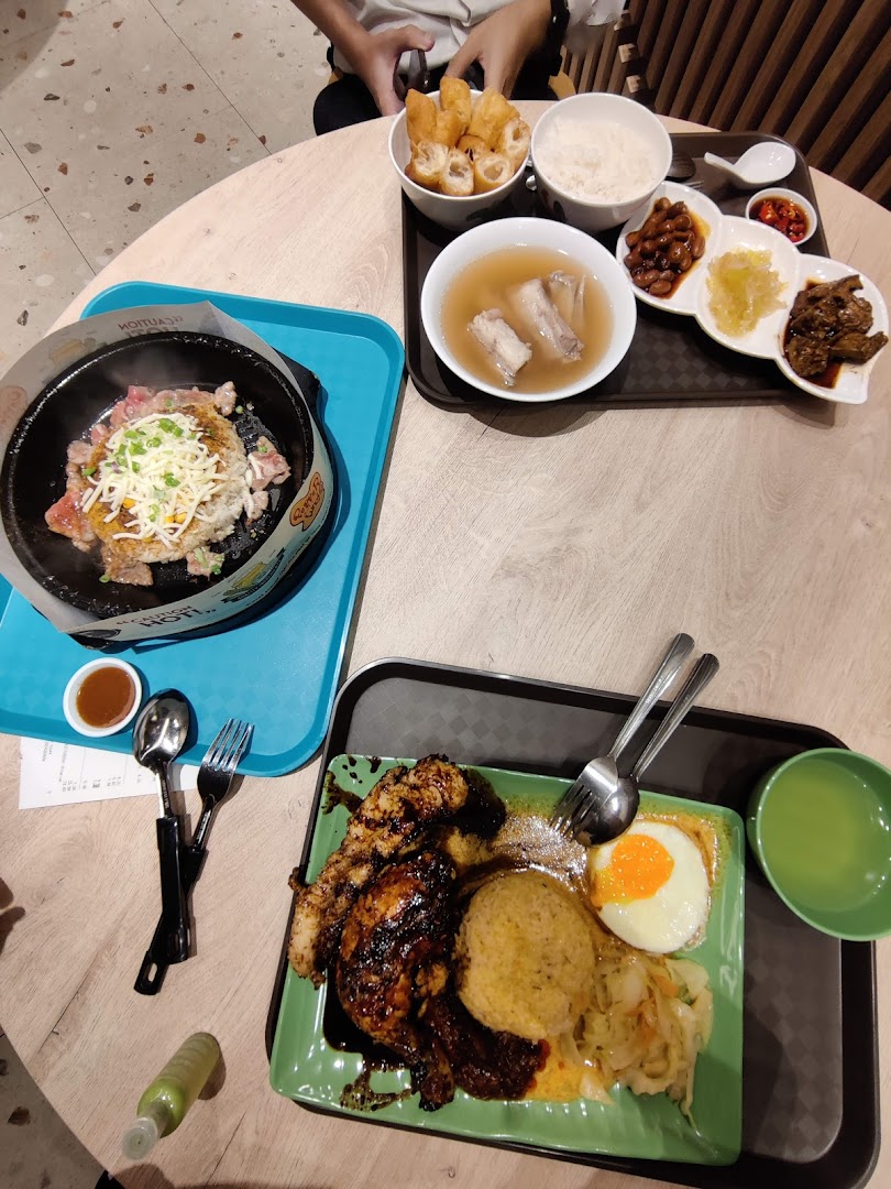 A table laden with various Indonesian dishes, including grilled chicken, rice, soup, and a sizzling plate.