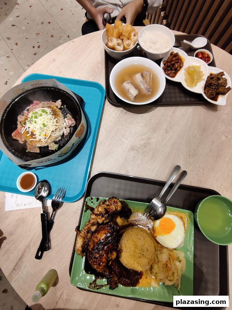 A table laden with various Indonesian dishes, including grilled chicken, rice, soup, and a sizzling plate.