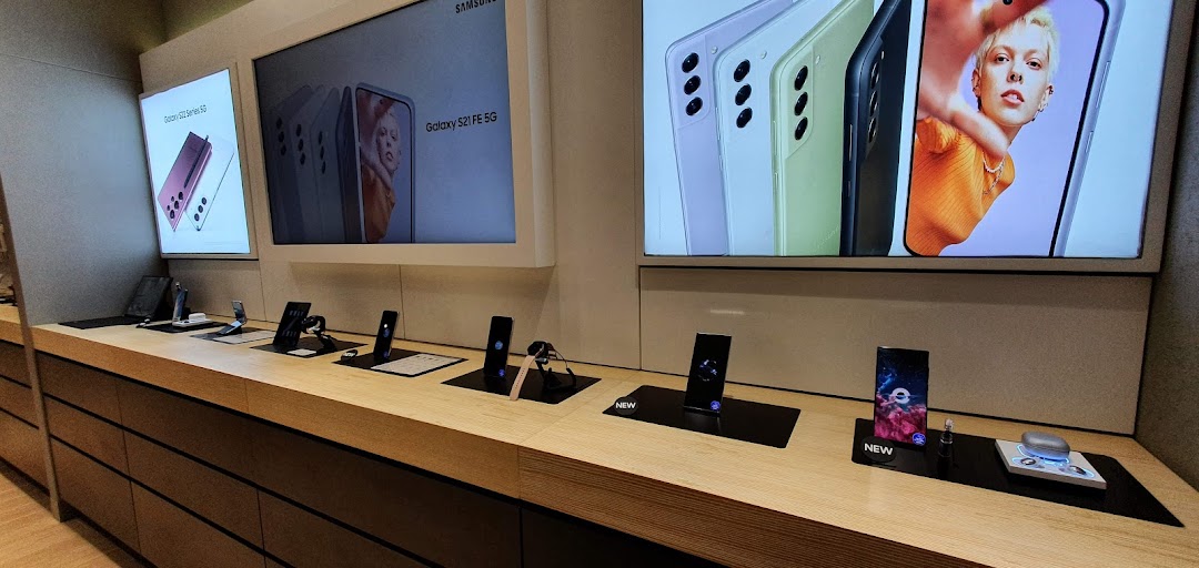 A display of Samsung smartphones and smartwatches with large promotional screens in a modern retail setting.
