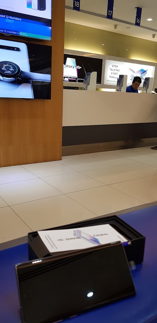 Interior view of a Samsung Service Centre with product displays, a service counter, and a staff member.