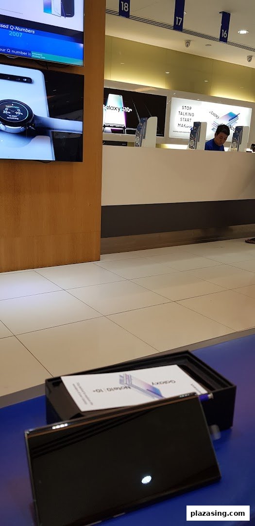 Interior view of a Samsung Service Centre with product displays, a service counter, and a staff member.