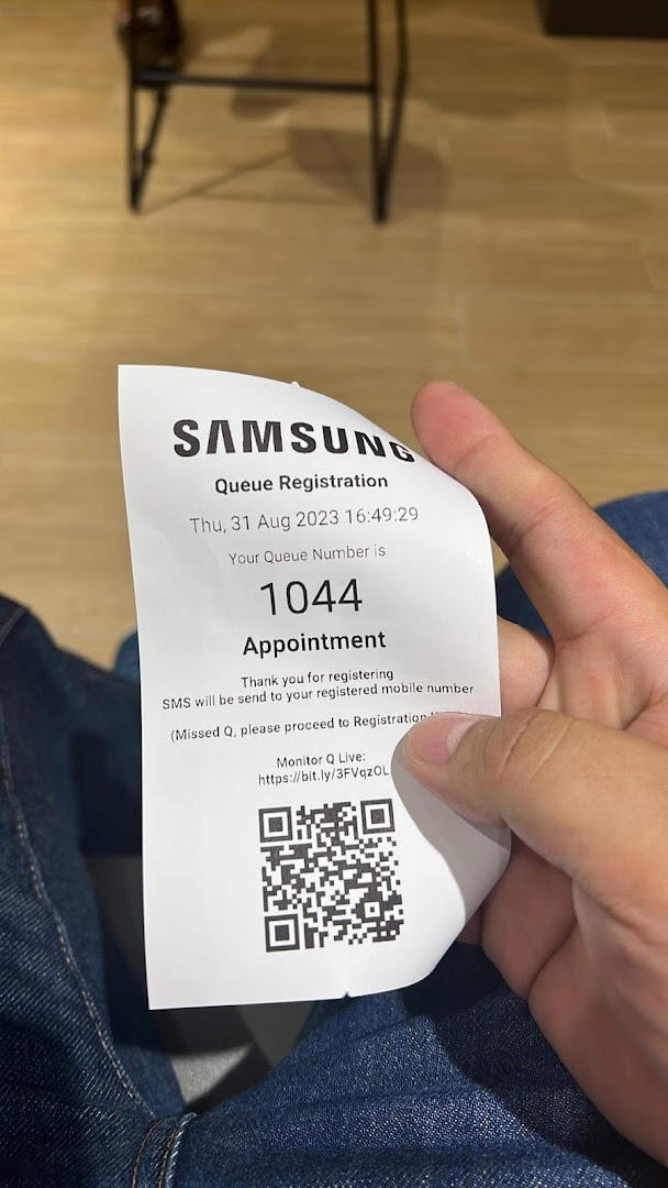 A person holds a Samsung Service Centre queue registration ticket with number 1044.