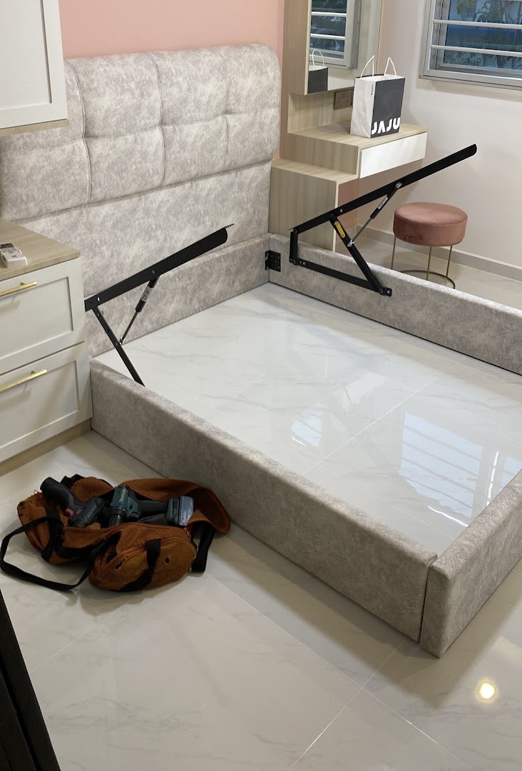 A partially assembled upholstered bed frame with a headboard and tools on a tiled floor.