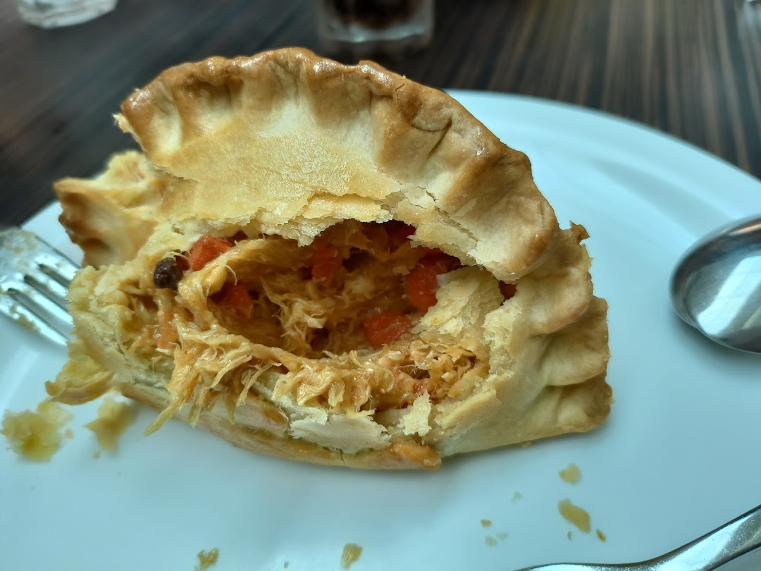A close-up of a savory pie or pastry with a flaky crust, revealing a rich, shredded chicken filling.