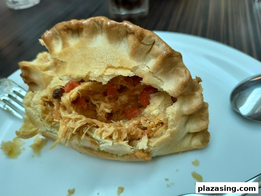 A close-up of a savory pie or pastry with a flaky crust, revealing a rich, shredded chicken filling.