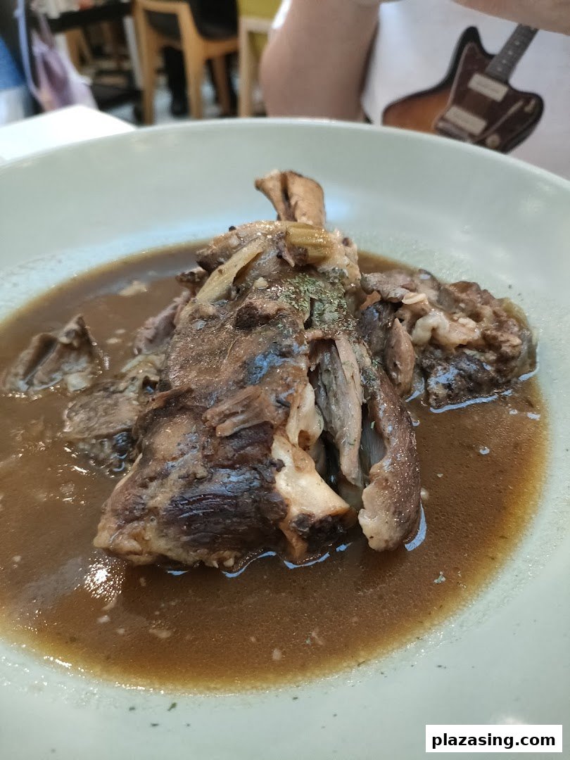 A close-up of a hearty braised meat dish, possibly lamb shank or oxtail, in a rich brown gravy.