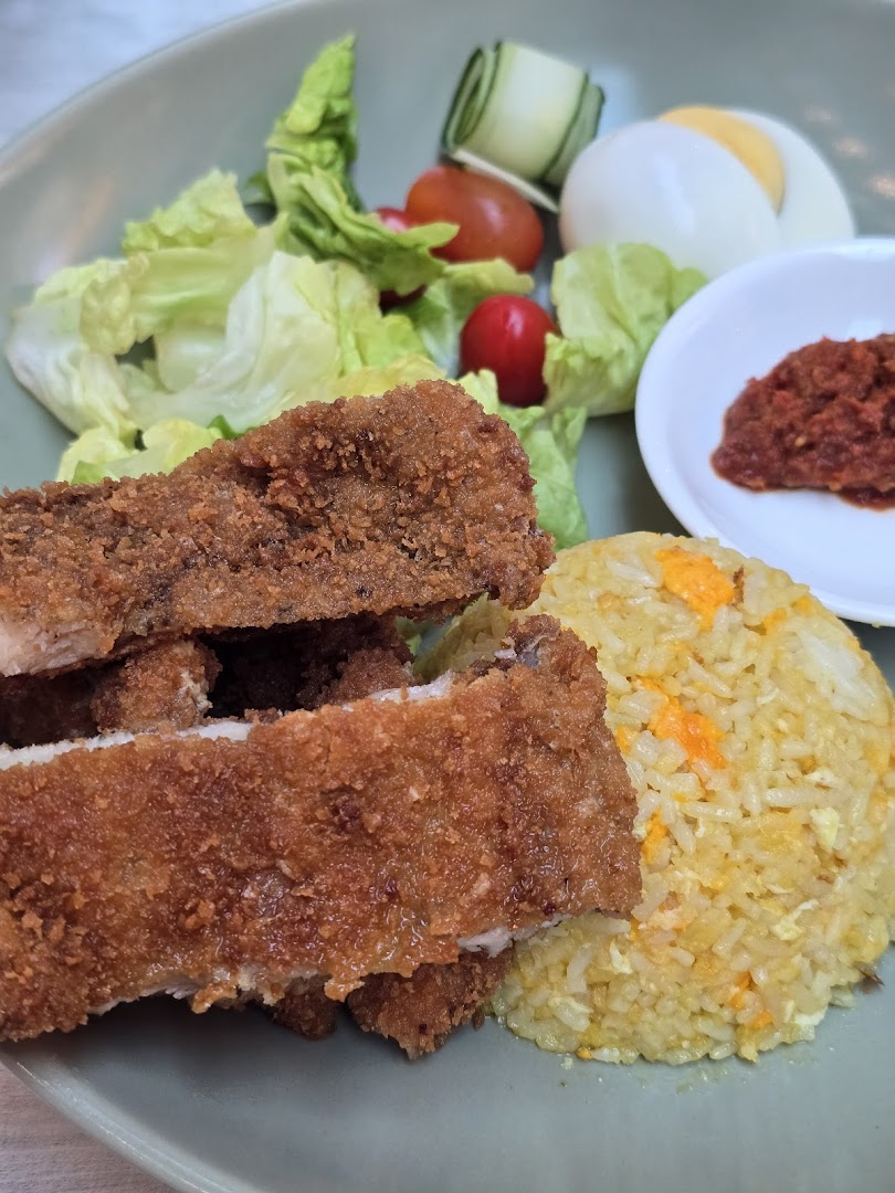 A plate of crispy fried chicken cutlets with savory fried rice, fresh salad, and a side of chili paste.