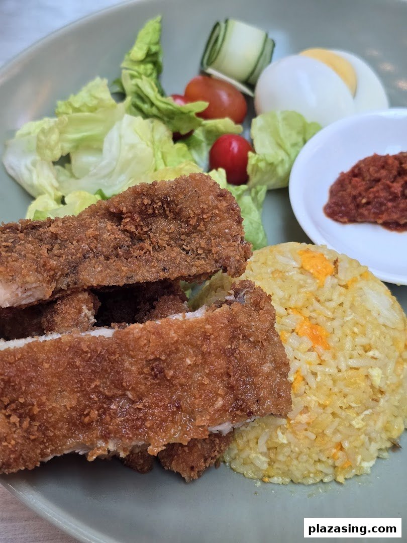 A plate of crispy fried chicken cutlets with savory fried rice, fresh salad, and a side of chili paste.