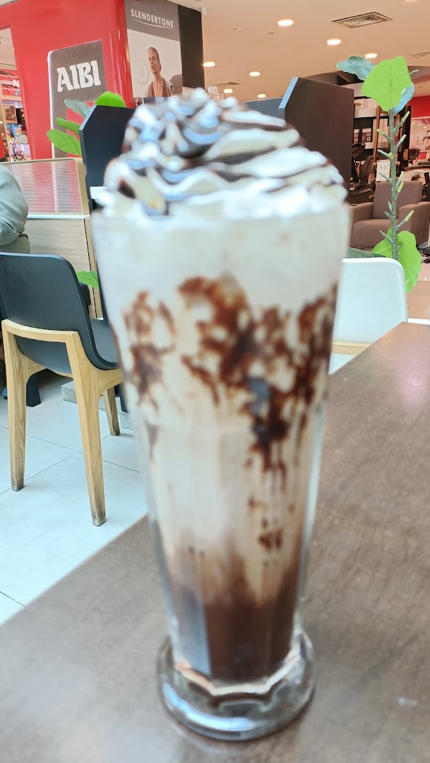A tall glass of chocolate milkshake topped with whipped cream and chocolate drizzle.