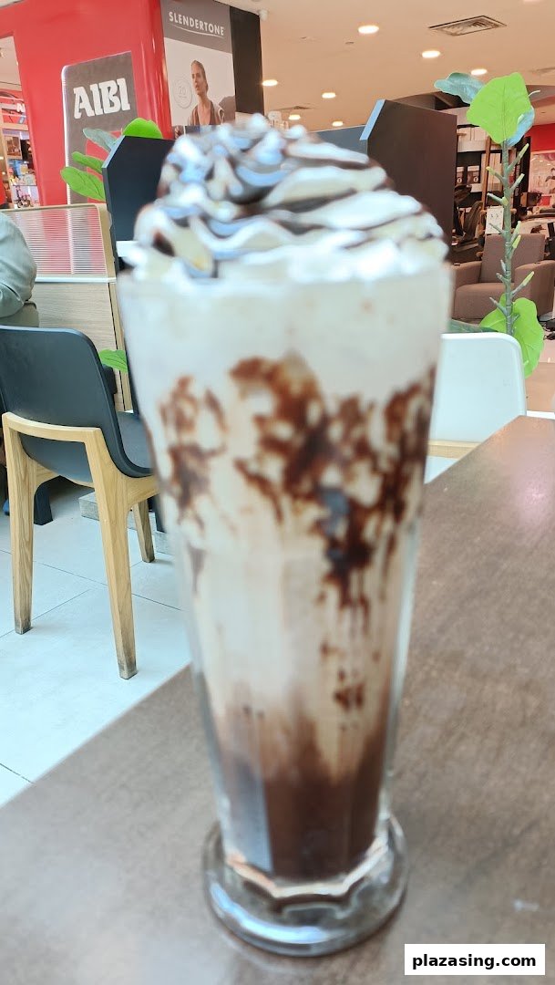 A tall glass of chocolate milkshake topped with whipped cream and chocolate drizzle.