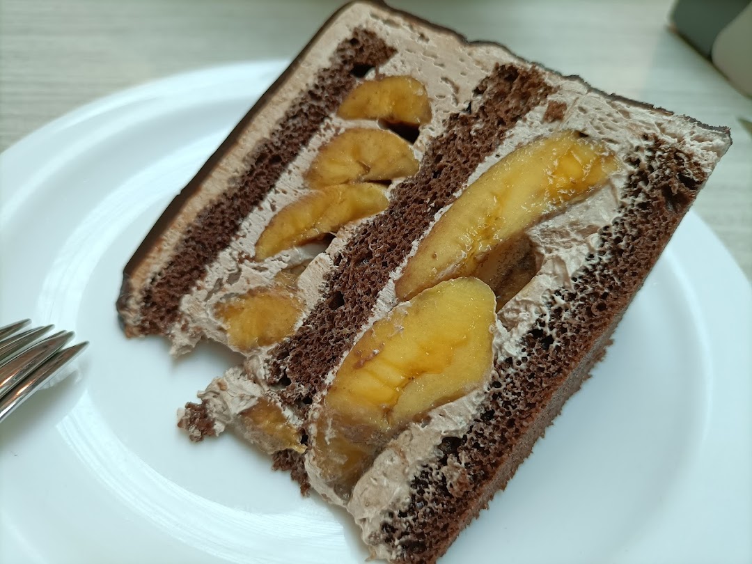 A delicious slice of chocolate cake with banana filling and creamy frosting on a white plate.
