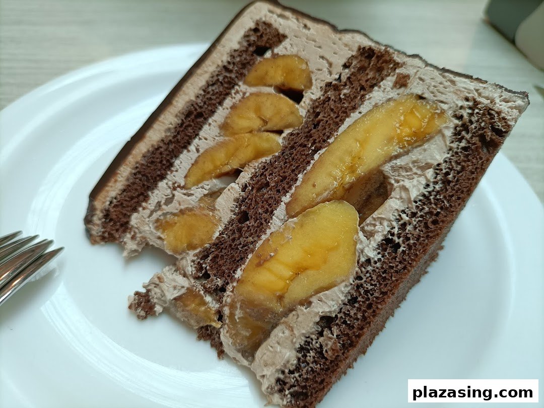 A delicious slice of chocolate cake with banana filling and creamy frosting on a white plate.