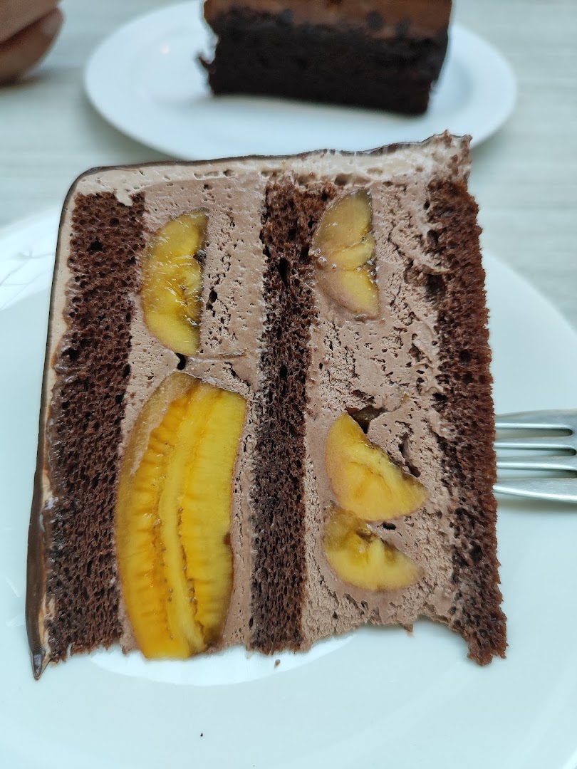A delicious slice of chocolate banana cake with creamy chocolate frosting on a white plate.
