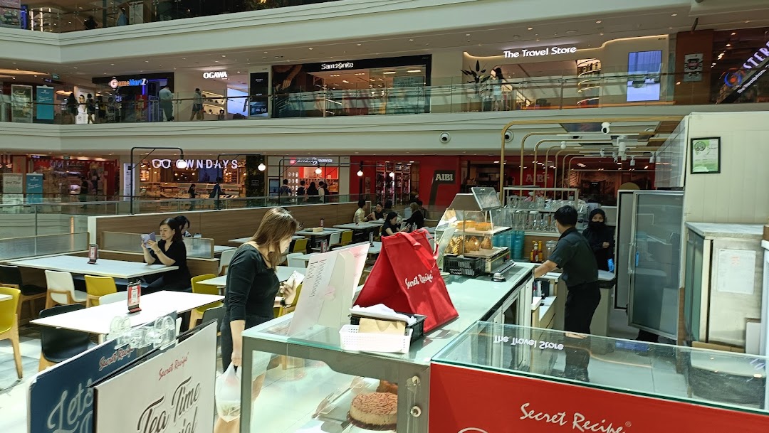 A bustling mall interior featuring Secret Recipe cafe with customers, counter, and surrounding shops.