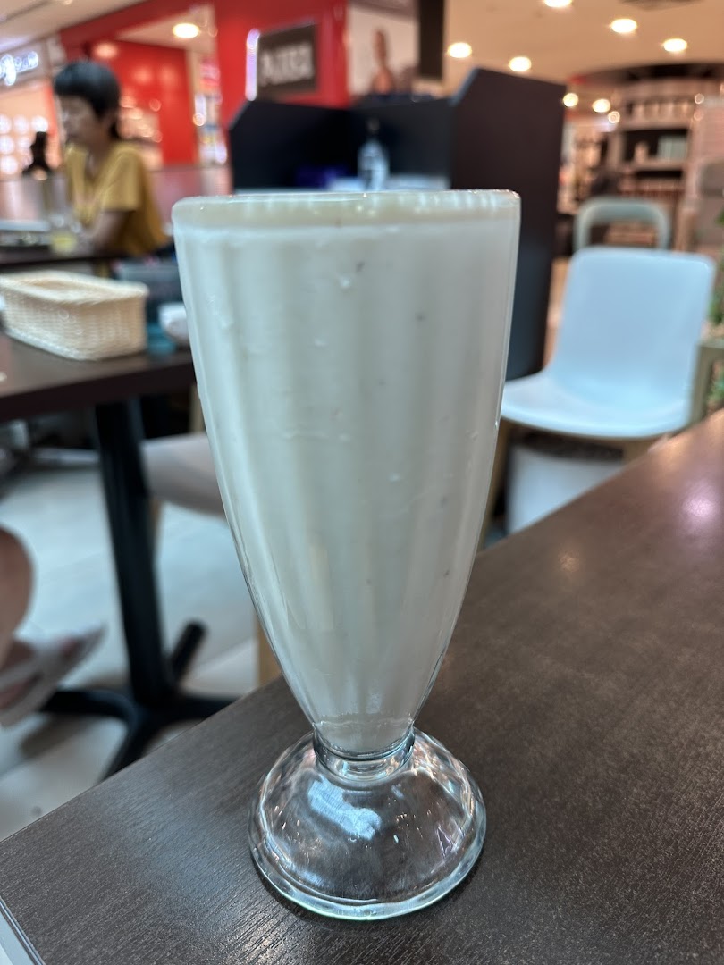 A tall glass of creamy white beverage, likely a milkshake or smoothie, on a dark table.