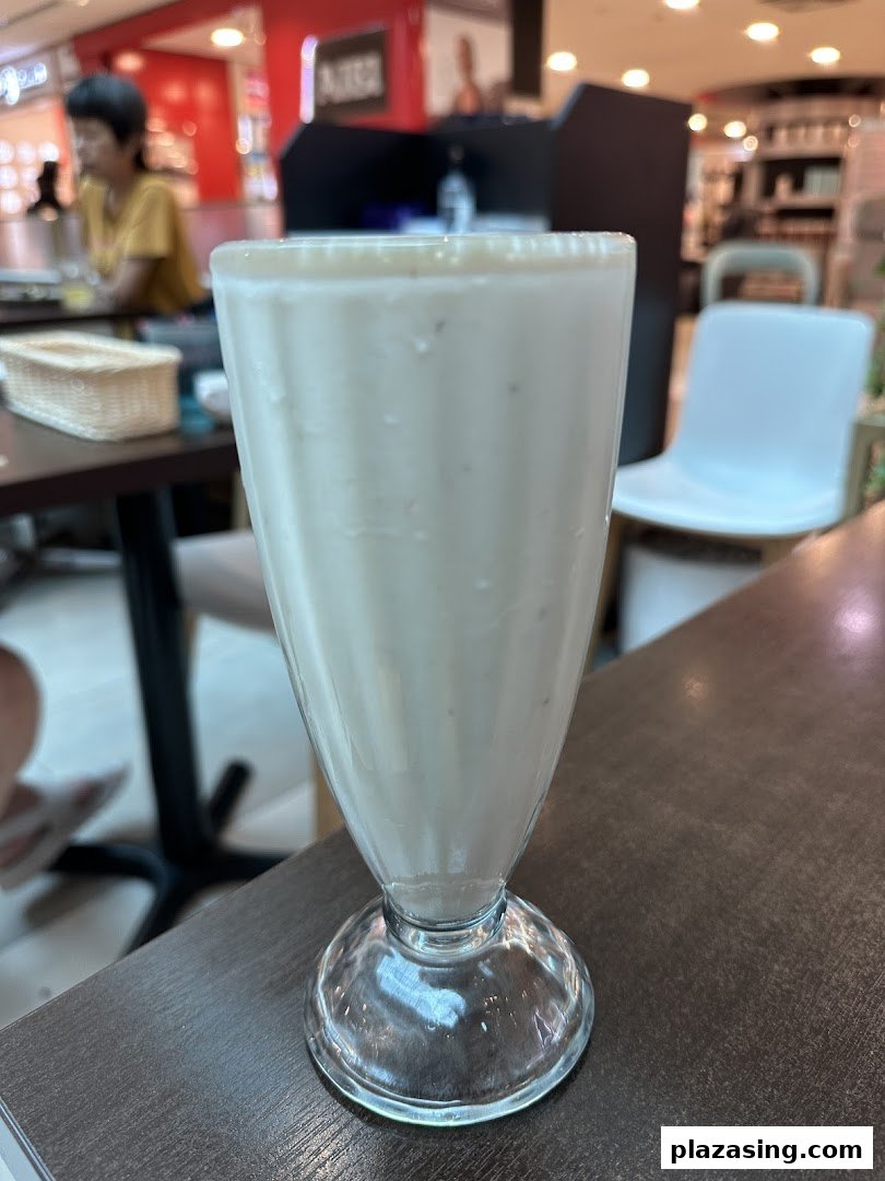 A tall glass of creamy white beverage, likely a milkshake or smoothie, on a dark table.