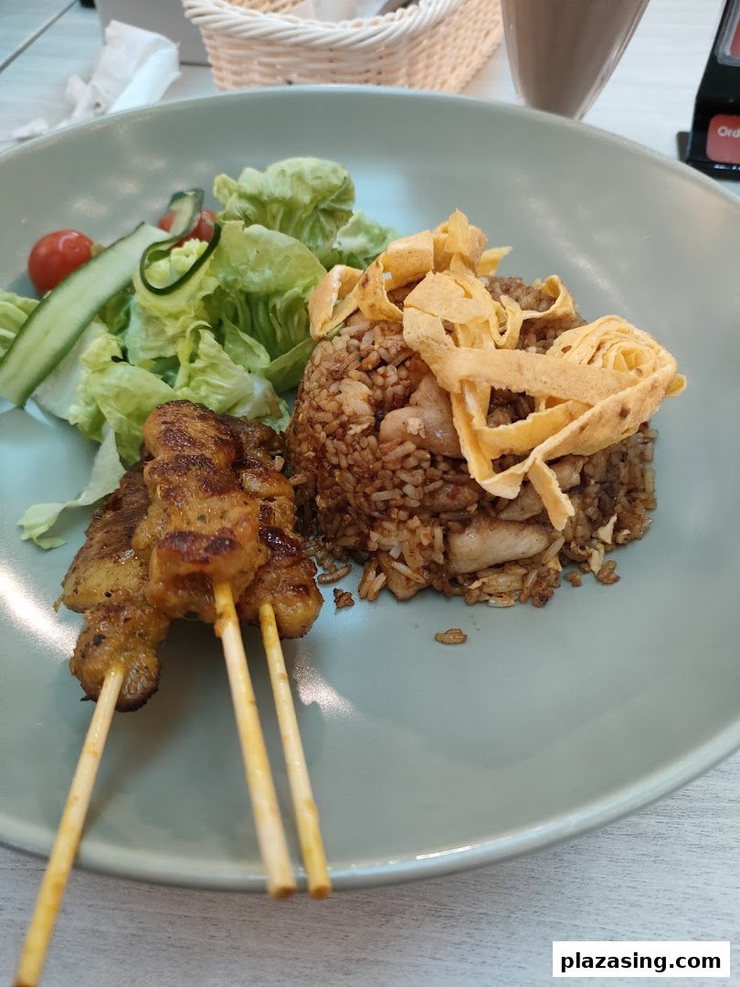 A plate of fried rice with chicken satay skewers and a fresh side salad.