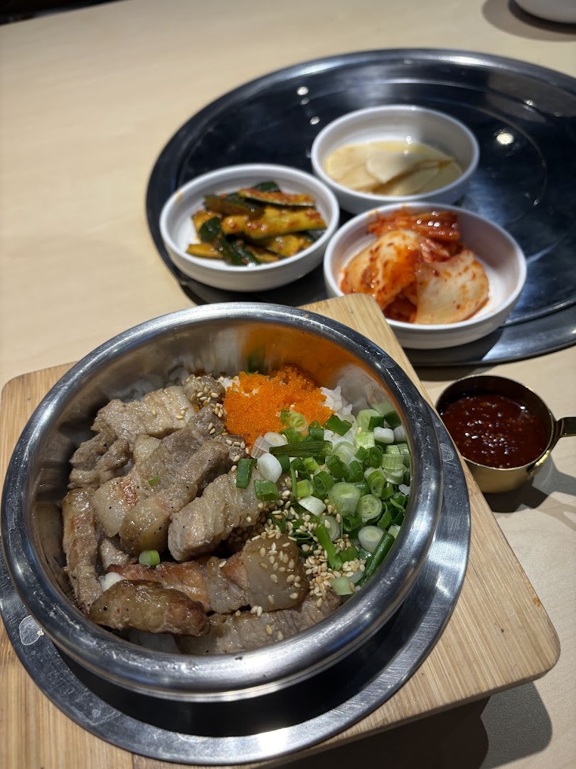 A delicious Korean rice bowl with grilled pork belly, roe, and fresh spring onions, served with banchan.