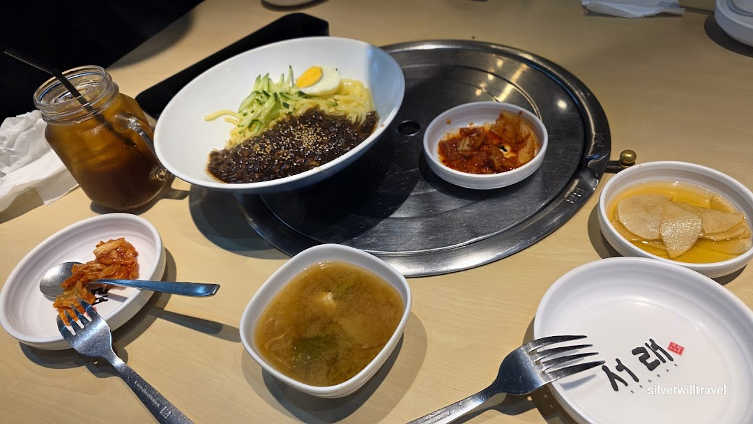A vibrant spread of Korean dishes, including Jajangmyeon, kimchi, and banchan, on a dining table.