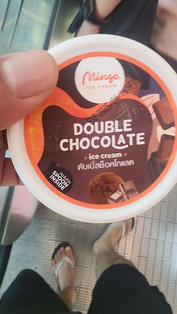 A hand holds a Mingo Double Chocolate ice cream cup, featuring its label and 'spoon inside' detail.