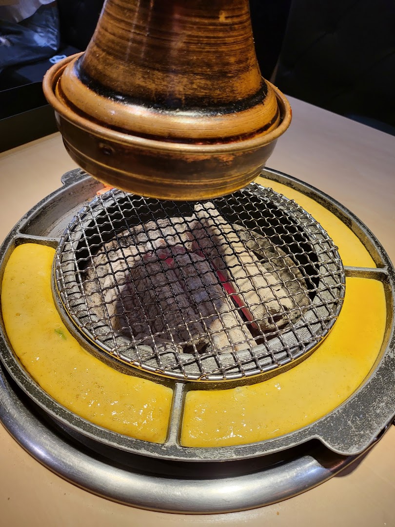Close-up of a Korean BBQ grill with hot charcoal and cooking egg mixture, ready for grilling.