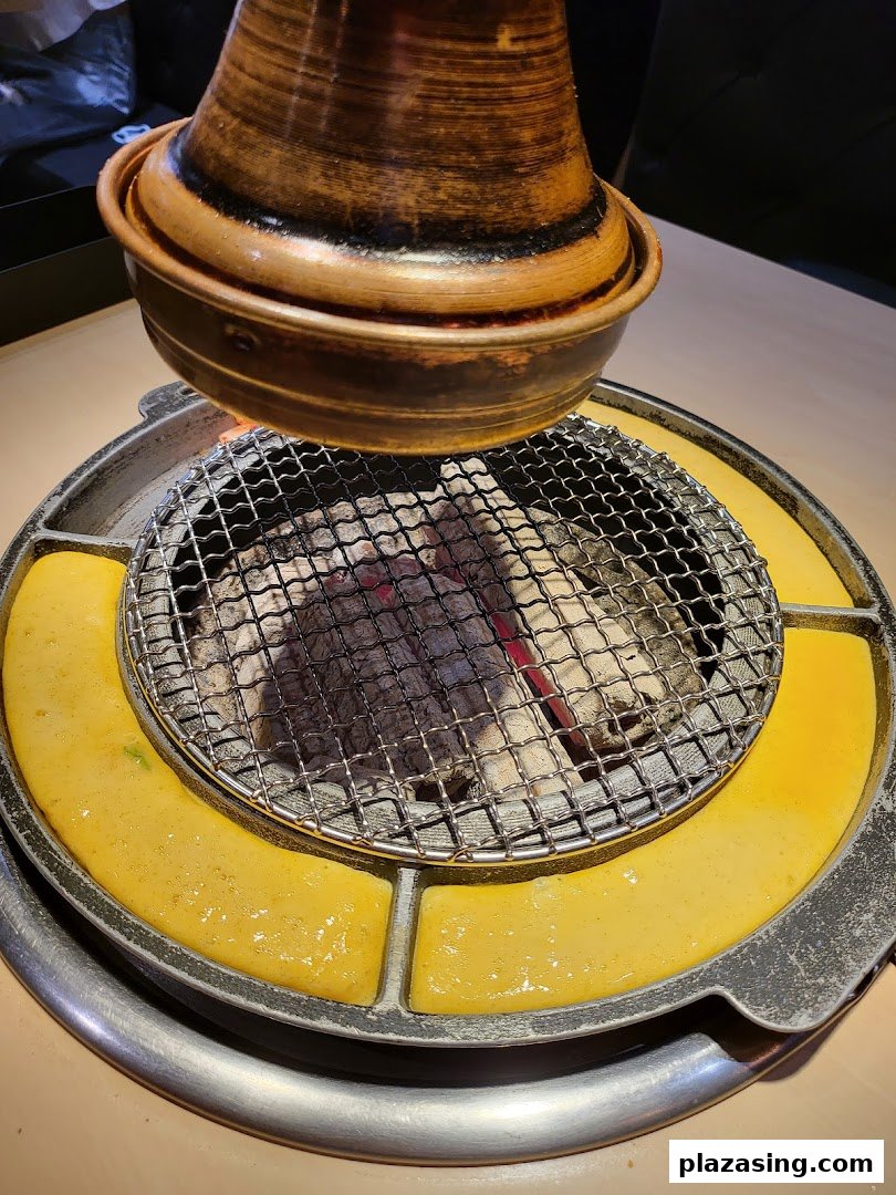 Close-up of a Korean BBQ grill with hot charcoal and cooking egg mixture, ready for grilling.