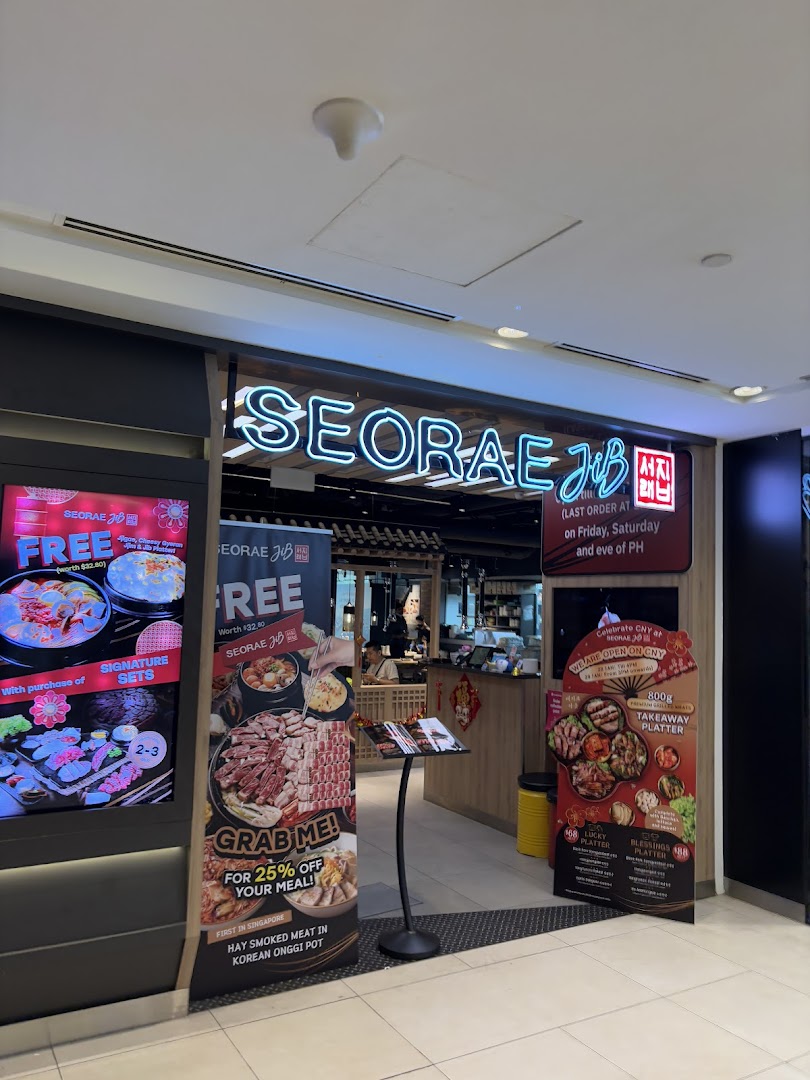The vibrant entrance of Seorae Jib, a Korean BBQ restaurant, featuring neon signage and promotional displays.