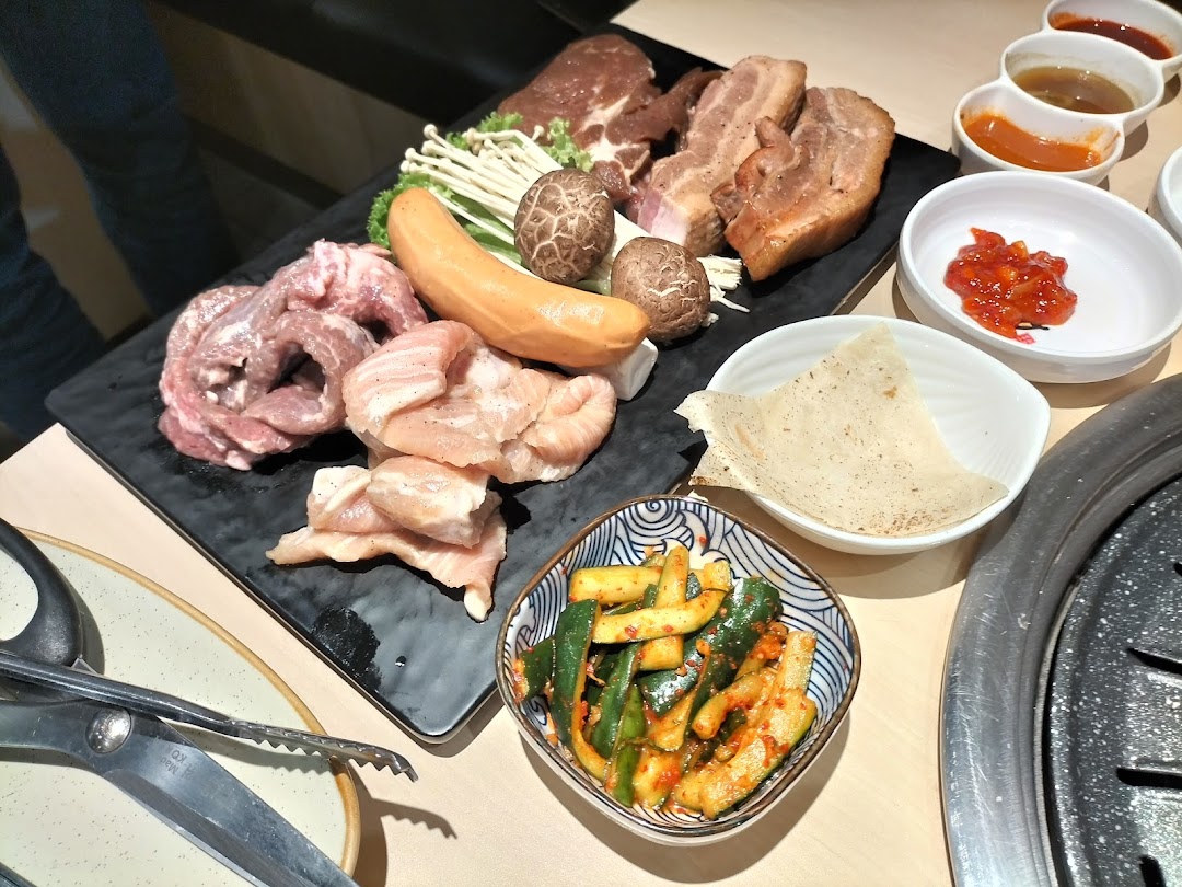A vibrant platter of raw meats, sausage, mushrooms, and side dishes ready for grilling at a Korean BBQ restaurant.