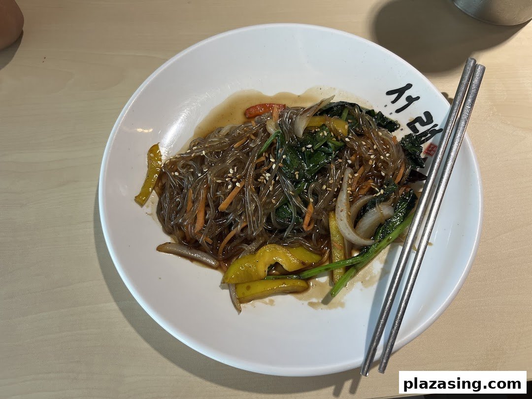 A delicious plate of Korean glass noodles (Japchae) with vegetables and chopsticks.
