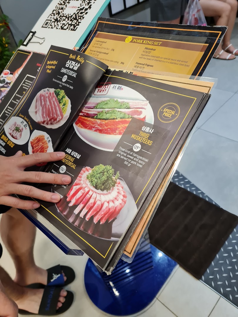 A close-up view of a Korean BBQ restaurant's menu, showcasing various pork dishes and sets.