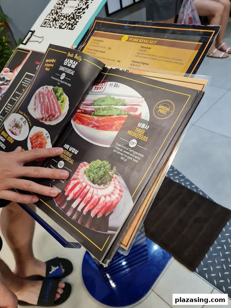 A close-up view of a Korean BBQ restaurant's menu, showcasing various pork dishes and sets.