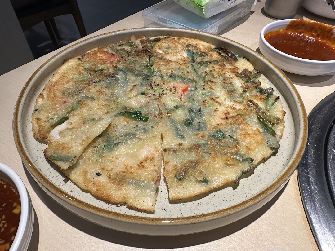 A delicious Korean seafood pancake (Pajeon) served on a plate with dipping sauces.