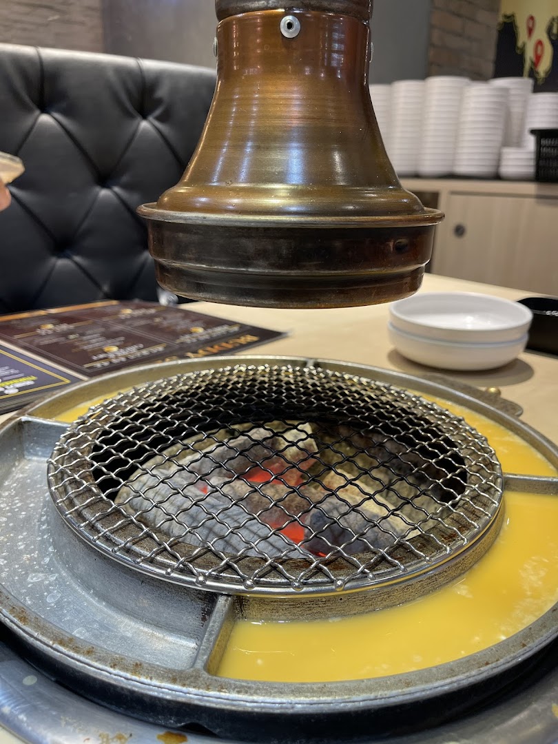 Close-up of a Korean BBQ grill with glowing charcoal and a side moat for cooking egg or cheese.