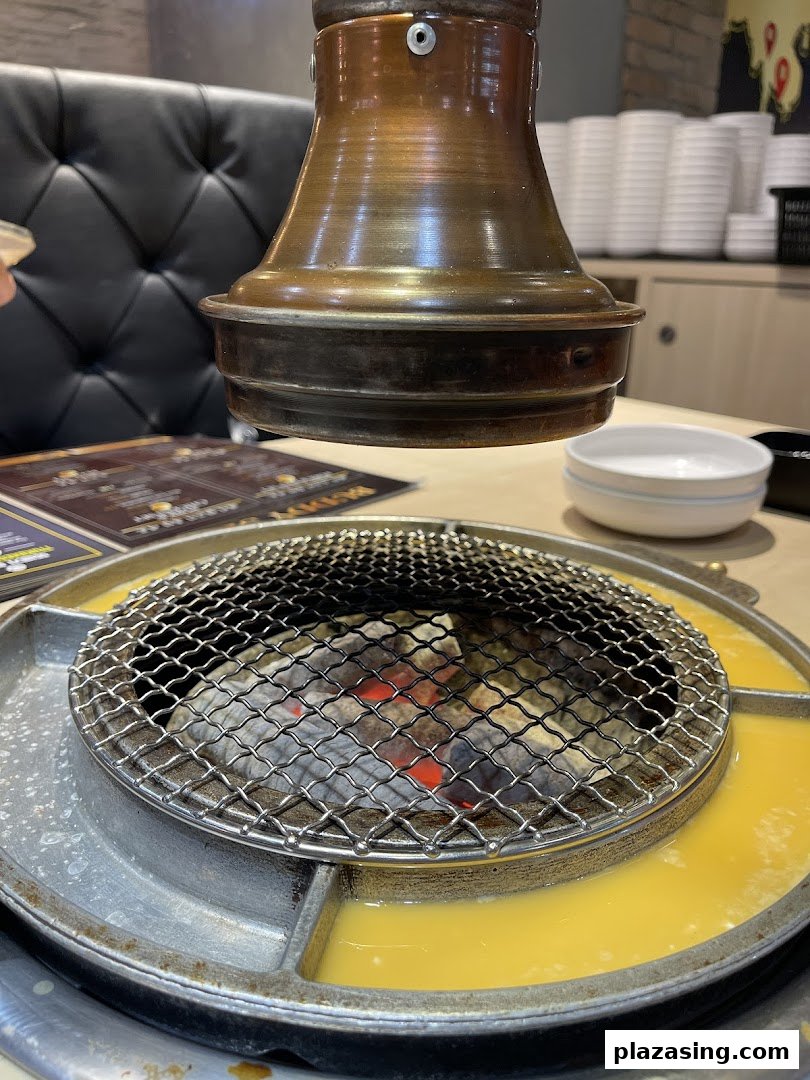 Close-up of a Korean BBQ grill with glowing charcoal and a side moat for cooking egg or cheese.