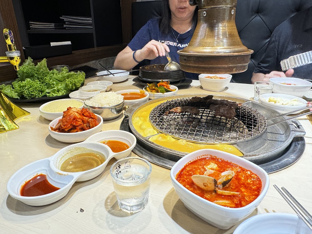 A vibrant table spread at a Korean BBQ restaurant, featuring grilled meat, various side dishes, and diners.