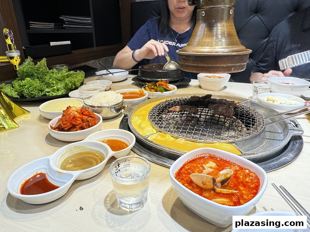 A vibrant table spread at a Korean BBQ restaurant, featuring grilled meat, various side dishes, and diners.