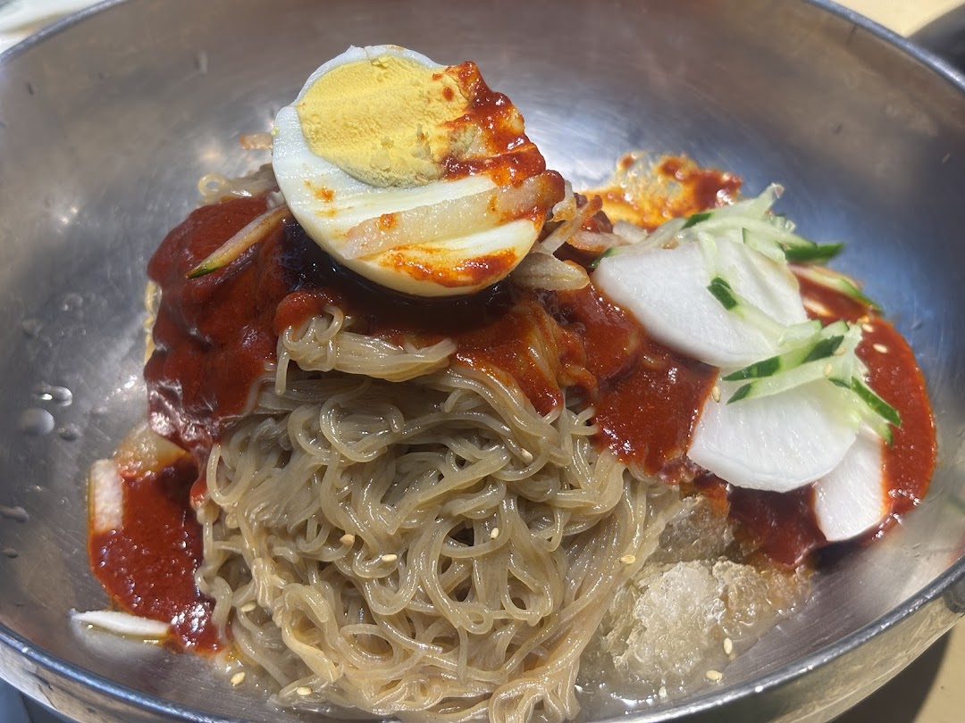 A close-up of Korean spicy cold noodles (Bibim Naengmyeon) with a boiled egg and pickled radish.