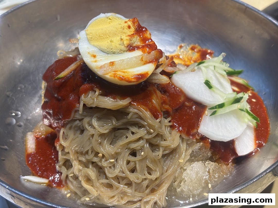 A close-up of Korean spicy cold noodles (Bibim Naengmyeon) with a boiled egg and pickled radish.