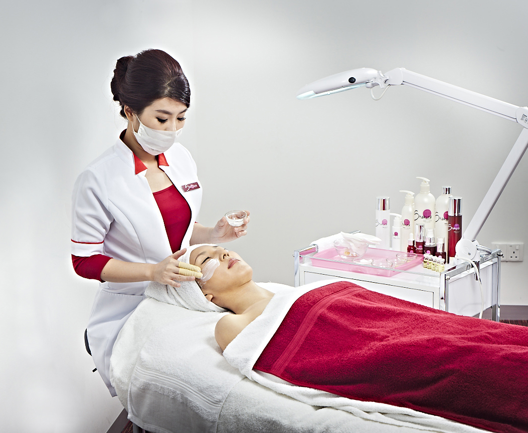 A beauty therapist applies a facial treatment to a client in a clean, professional setting.