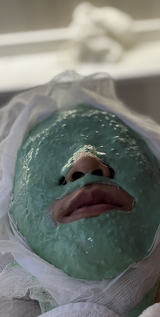 A person receiving a green facial mask treatment at Shakura Pigmentation Beauty.